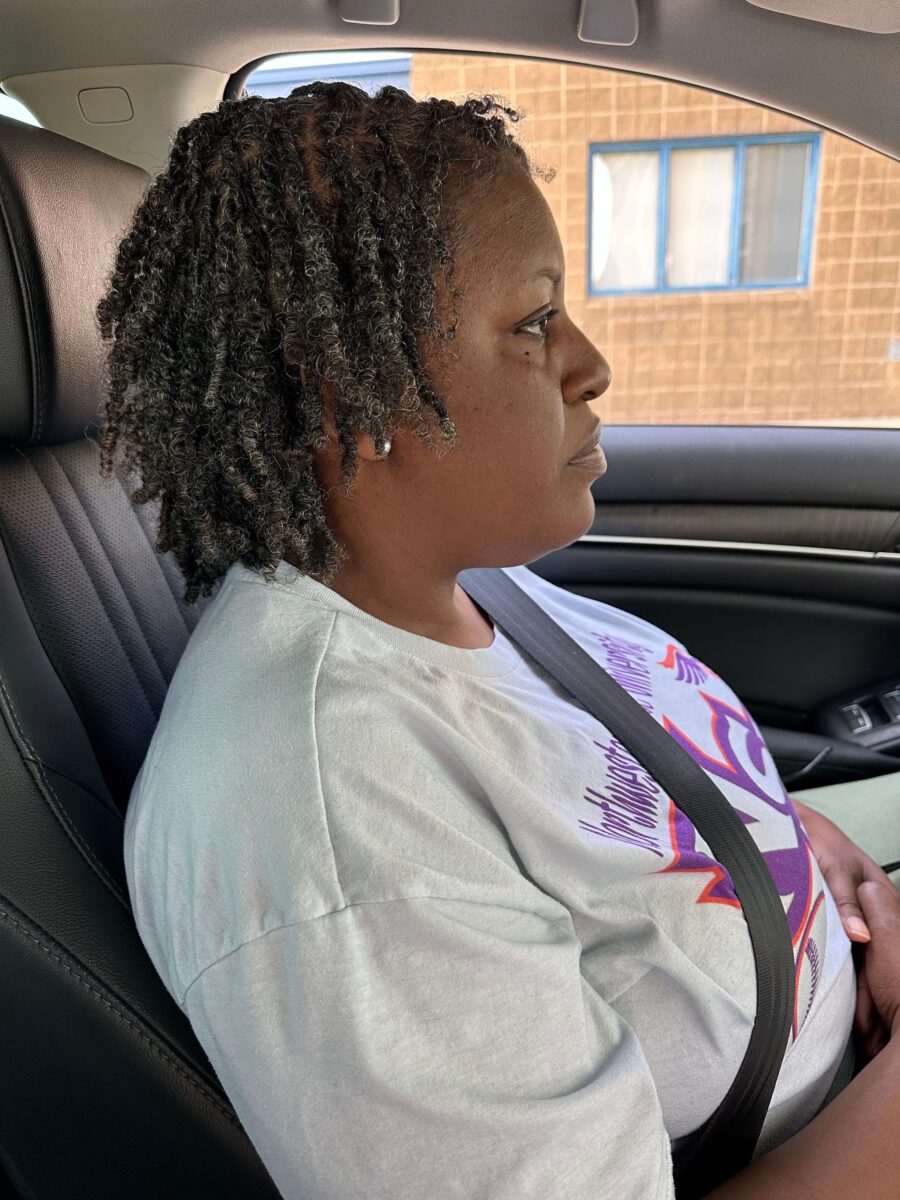Side profile of a woman sitting in a car wearing a white graphic T-shirt, with twisted natural hair styled neatly